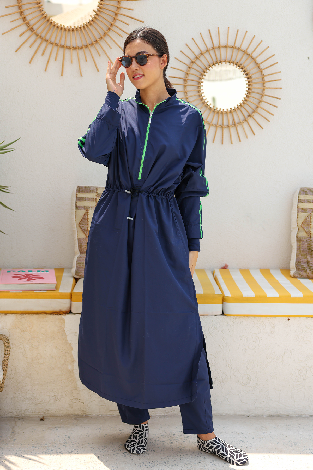 Woman wearing a navy blue outfit with a green zipper in a sunlit room.