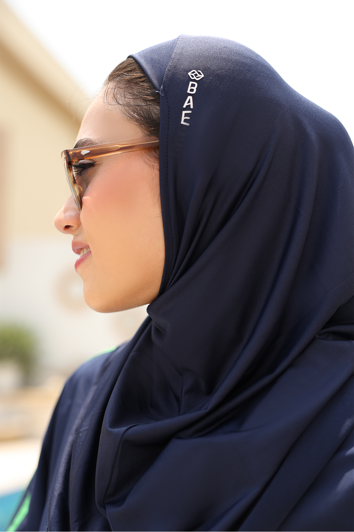 Woman wearing a navy hijab with a brand logo, outdoors.