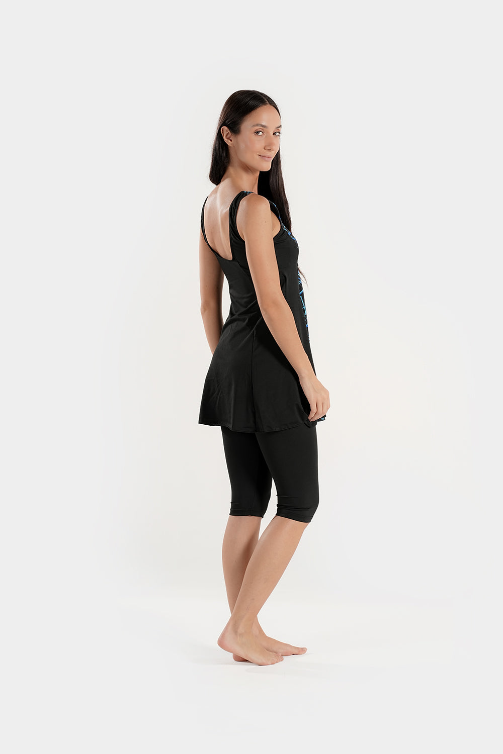 Woman wearing a black sleeveless top and black capri leggings on a white background